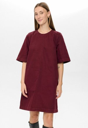 Robe en coton bourgogne à manches courtes, décolleté rond et coupe droite. Présente des coutures visibles et s'arrête au-dessus du genou.