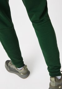 Pantalons de survêtement verts au design ajusté et en tissu texturé, associés à des chaussures vert olive avec un col rembourré et des panneaux texturés.
