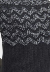 Chaussette en laine noire avec un motif en zigzag gris sur le dessus. Le design présente une texture lisse avec un ajustement confortable.