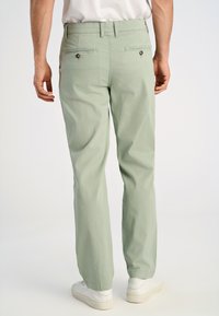 Jasnozielone bawełniane spodnie o prostym kroju, z dwiema tylnymi kieszeniami z guzikami oraz wygodnym pasem. W połączeniu z białymi trampkami.