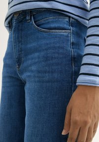 Světle modrá a tmavě modrá pruhovaná košile s dlouhým rukávem v klasickém střihu, doplněná modrými džínami s tradičním designem pěti kapes.