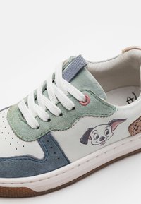 Sneaker multicolore con una base in pelle bianca, sovrapposizioni in suede blu e verde, caratterizzata da una stampa di un cane dei cartoni animati sul lato e lacci bianchi.