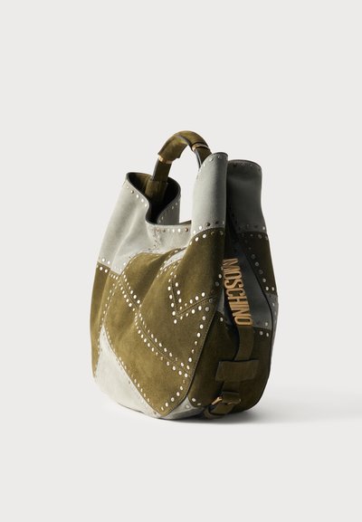 Πράσινη και γκρι σουέντ τσάντα ώμου με διακοσμητικά καρφιά και λογότυπο «Moschino» στο πλαϊνό λουρί, εμφανίζεται σε λευκό φόντο.