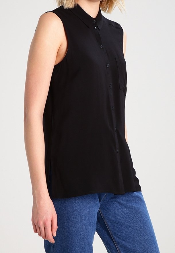 Blouse noire sans manches avec devant boutonné, col et poche poitrine. Tissu doux à la texture lisse, design simple et classique.