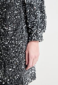 Vestido cinza texturizado coberto de lantejoulas, com um tecido suave e mangas ligeiramente bufantes, destacando detalhes intrincados e brilho.
