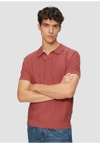 Rostfarbendes Polohemd mit V-Ausschnitt, kurzen Ärmeln, geripptem Kragen und Saum, aus strukturiertem Stoff gefertigt. Sichtbares Logodetail an der Seite.