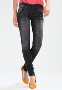 Los jeans skinny negros tienen un ajuste ceñido y un desvanecimiento mínimo, combinados con tacones de aguja de ante naranja. El conjunto tiene una apariencia casual pero pulida.