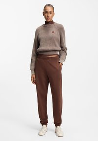 Brun ribstrikket sweater med høj hals og broderet logo, kombineret med brune sweatpants med manchetter ved anklerne og logo broderi.
