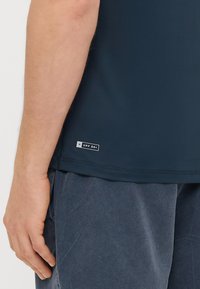 Mörkblå kortärmad skjorta i slät tyg, med en UPF 50+-etikett vid fållen, i kombination med mörkgrå, strukturerade shorts.