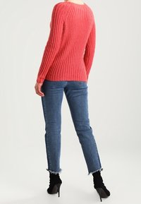 Pull côtelé rose à manches longues, associé à un jean bleu taille haute avec des ourlets effilochés et des bottines à talons noires.