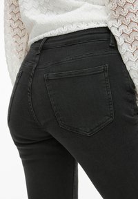 Zwarte denim jeans met een slim fit ontwerp. Voorzien van twee achterzakken en een stijlvolle, gladde textuur. Gecombineerd met een witte, gemusterde top.