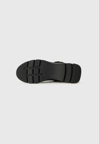 Sort skosål med tekstureret greb, der har vandrette riller og en let hæl. Glat materiale med et solidt design.