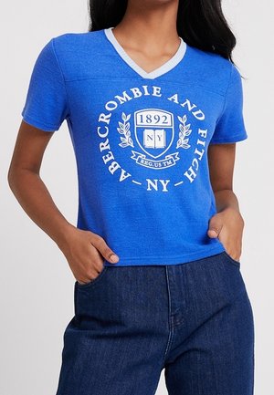 Blauw T-shirt met korte mouwen en V-hals, met een wit grafisch logo met de tekst "Abercrombie and Fitch," een schild en lauwerkransen. Zachte textuur.