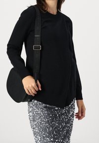 Černý pletený svetr, volný střih, ribbované manžety. Lesklá stříbrná sukně posetá flitry. Černá crossbody taška s logem. Hladké textury.