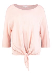 Top rosa chiaro a maniche corte con una vestibilità rilassata e dettagli legati davanti. Il materiale sembra morbido con una superficie liscia e un ampio scollo.