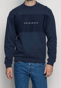 Felpa blu navy con pannello testurizzato e testo "ORIGINALS" in bianco. Collo tondo e maniche lunghe, realizzata in un misto cotone. Vestibilità casual.