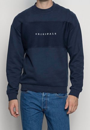 Sudadera de color azul marino con panel texturizado que presenta el texto "ORIGINALS" en blanco. Cuello redondo y mangas largas, fabricada en una mezcla de algodón. Corte casual.
