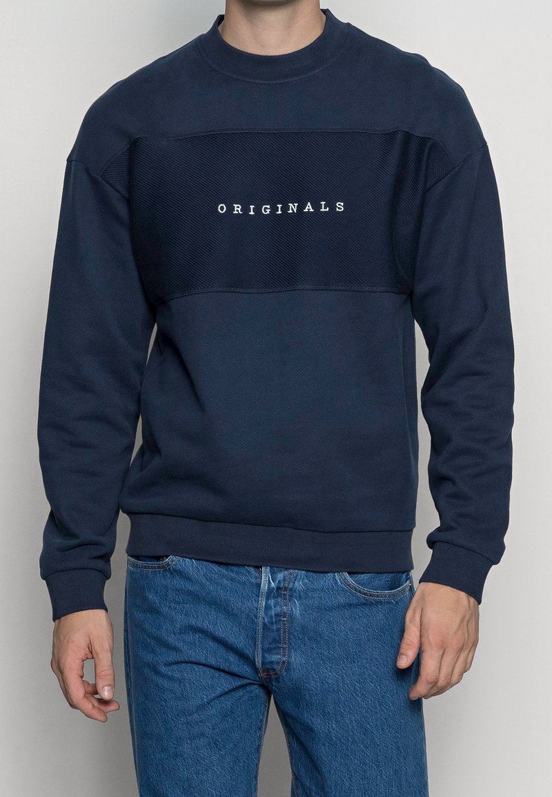 Felpa blu navy con pannello testurizzato e testo "ORIGINALS" in bianco. Collo tondo e maniche lunghe, realizzata in un misto cotone. Vestibilità casual.