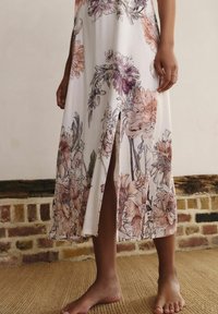 Abito midi floreale in tessuto morbido e leggero con sfondo bianco e motivi floreali in viola e pesca. Presenta uno spacco laterale.