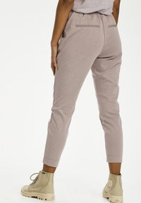 Hellbraune, taillierte Jogginghosen mit einem elastischen Bund, ausgestattet mit zwei Gesäßtaschen und kombiniert mit khakifarbenen Knöchelschuhen. Glatte Textur.