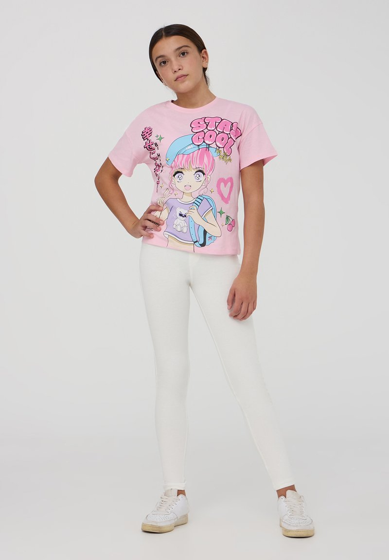 T-shirt rosa a maniche corte con illustrazione grafica, abbinato a leggings bianchi. La maglietta presenta un testo giocoso e dettagli di cartoni animati.