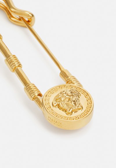 Gold safety pin brooch with a Medusa head design, intricate Greek key pattern, and polished finish. Features a tubular clasp and wrapped accents.