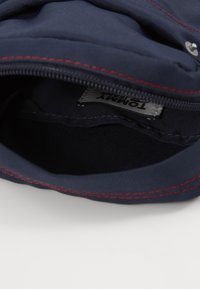 Interno di una borsa in tessuto navy con cuciture rosse, dotata di chiusura con zip e un'etichetta di Tommy Jeans. Texture liscia, senza motivi visibili.