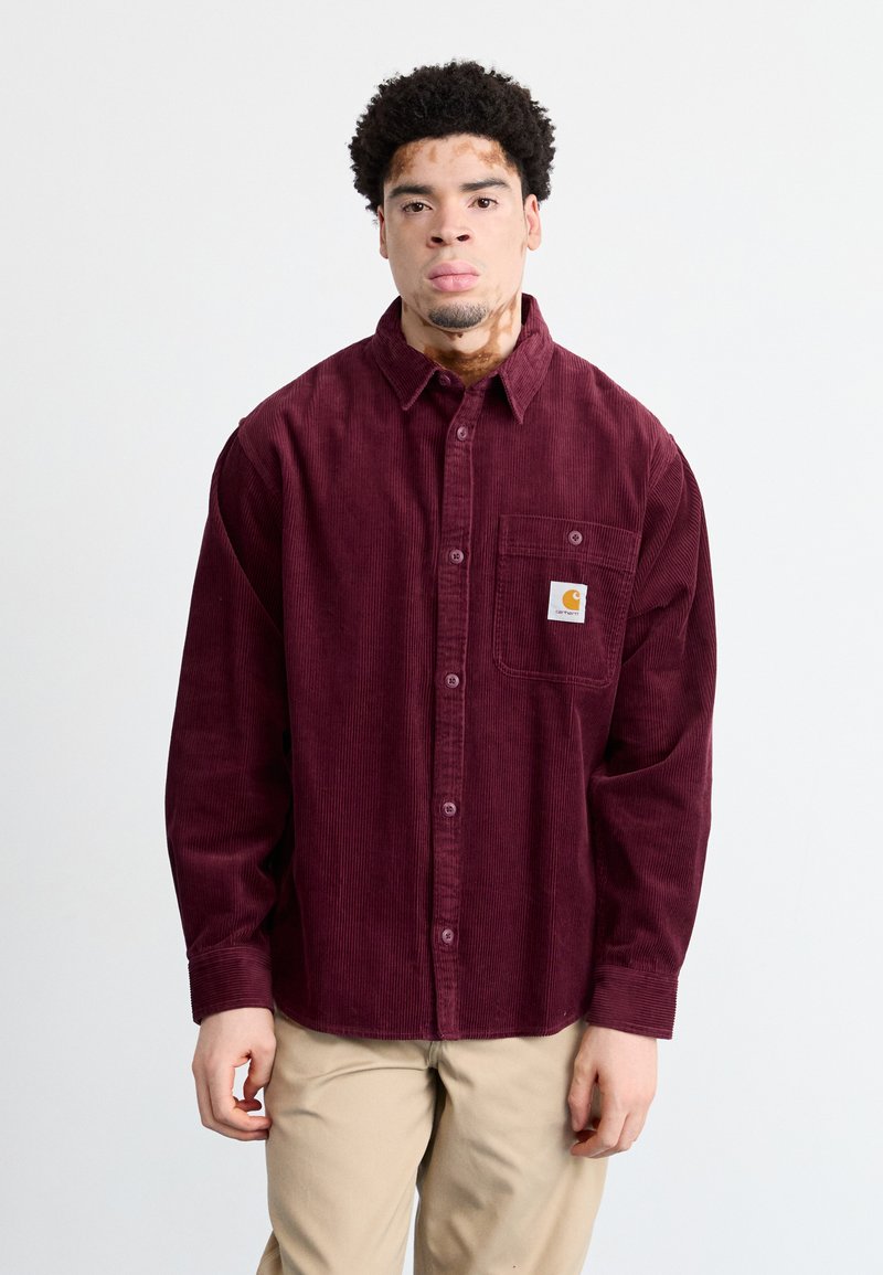 Burgundy kordfløjl skjorte med knapper, fra brystlommen og logo-patch, har en afslappet pasform og lange ærmer. Lyse beige bukser.
