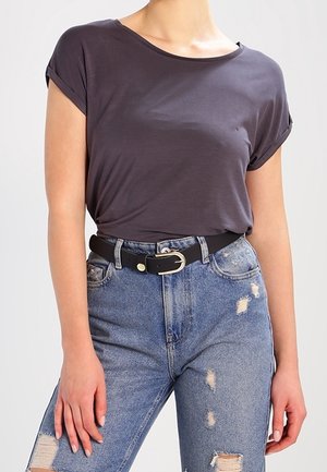Person wearing dark gray rolled-sleeve t-shirt tucked into ripped blue jeans with a black belt featuring a gold buckle.