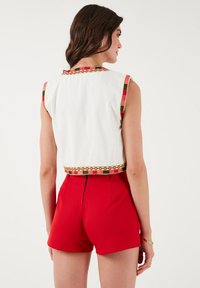 Crop top blanc avec un ourlet géométrique multicolore, associé à un short rouge taille haute, comportant une fermeture éclair dissimulée au dos.