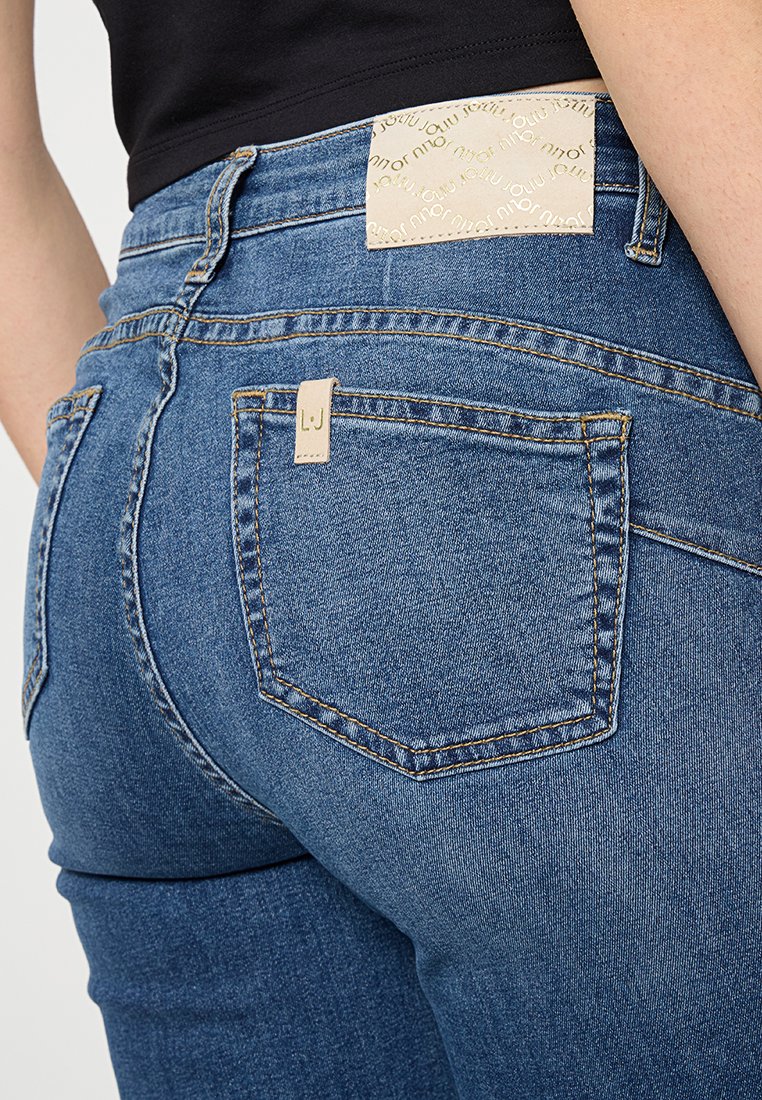 Blaue Denim-Jeans mit einer eng anliegenden Passform, ausgestattet mit einem beigen Etikett auf der Gesäßtasche und Kontrastnähten.