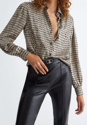 Femme portant un chemisier à motifs boutonné, rentré dans un pantalon en cuir noir taille haute avec une boucle de ceinture décorative.
