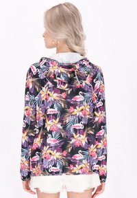 Huvtröja i svart tyg med ett livligt blommönster och flamingos. Har långa ärmar och en avslappnad passform, med dragsko i huvan.