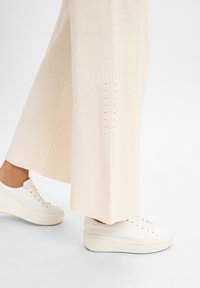 Cremfarbene, gerippte Hose mit weitem Bein und seitlichen Schlitzen sowie einem strukturierten Strickmuster, kombiniert mit beigen Plateausneakers.