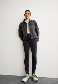 Veste en denim gris foncé, pull léger en tricot crème, jeans noirs taille haute et baskets beige-vert avec des accents de lacets.