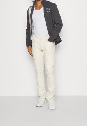 Harmaa vetoketjullinen takki logolla, valkoinen toppi, kermaiset housut ja valkoiset lenkkarit. Slim fit -leikkaus, sileä kangas ja minimalistinen muotoilu.