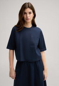 Marineblaue, kurze T-Shirt aus glattem Stoff mit rundem Halsausschnitt und kurzen Ärmeln, ausgestattet mit einer kleinen Tasche auf der linken Brust.