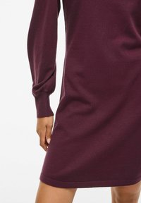 Vestido de punto burdeos con mangas largas, ligeramente abullonadas y un corte relajado, que presenta una textura suave y una longitud a medio muslo.