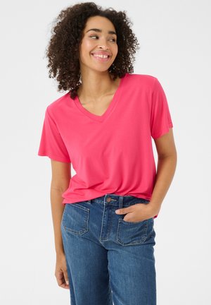 T-shirt rose à col en V en tissu doux, coupe décontractée, manches courtes, associé à un jean bleu taille haute avec poches visibles et bouton.