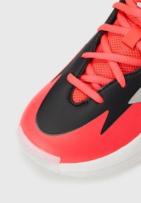 Baskets de sport rouge vif et noires avec une tige en mesh texturé, lacets plats et semelle en caoutchouc. Dotées d'un bout pointu et d'accents de design épurés.