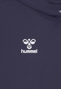 Mörkblå hoodie i mjukt tyg med en vit "hummel"-logotyp och ett distinkt bi-emblem. Klassisk modell med luva.