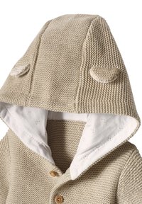Beige gestrickte Babyjacke mit Kapuze, die zwei kleine Stoffohren auf der Kapuze hat und innen mit weichem Weiß gefüttert ist.