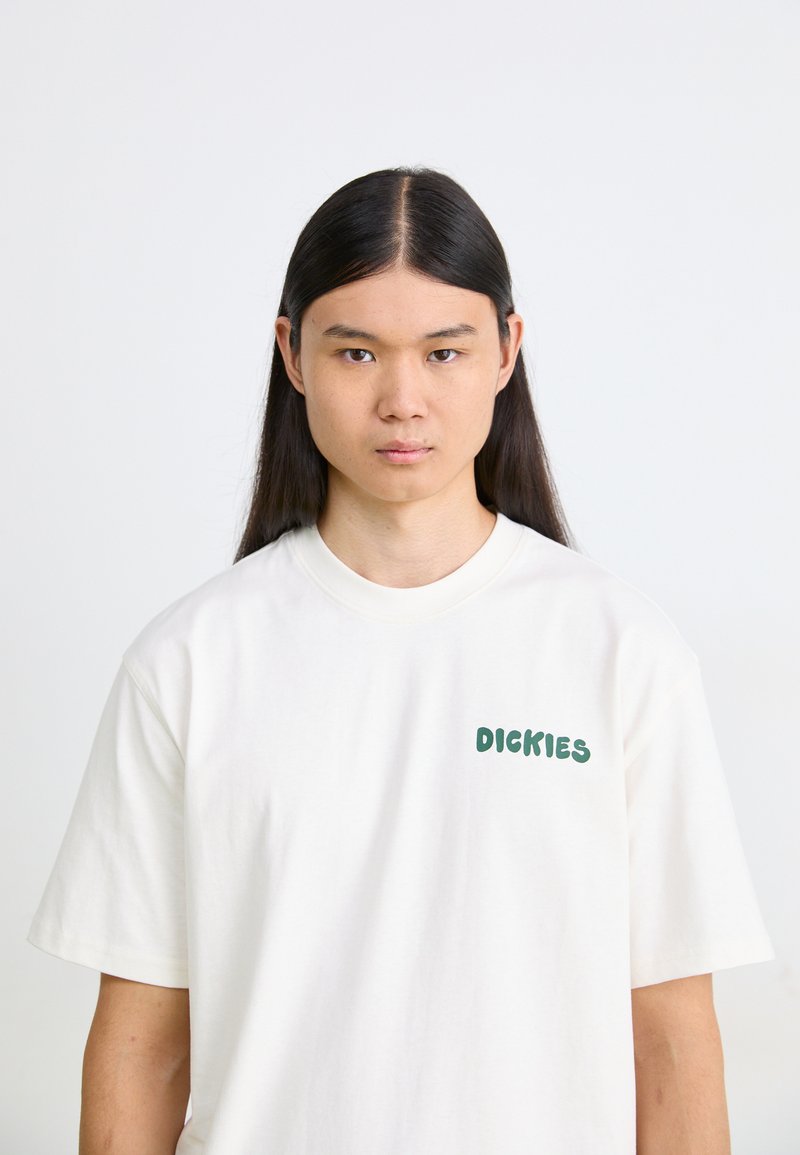 T-shirt bianco in cotone a maniche corte, con la scritta verde "DICKIES" nella zona sinistra del petto. Texture liscia, vestibilità classica.