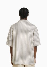 Kortärmad skjorta i ljusbeige med vertikala bruna ränder. Har en avslappnad passform, krage och texturerat tyg.