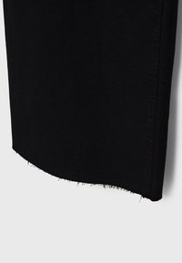Jupe en jean noire avec un ourlet brut et effiloché sur un fond gris uni.