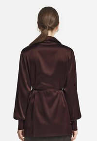 Långärmad, burgundy satinblus med bälte i midjan, avslappnad passform och slät textur med minimal detaljer.