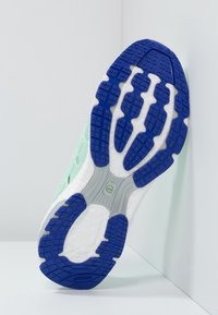 Podeszwa buta ma wzorzysty niebieski gumowy bieżnik, fakturowaną białą środkową część oraz miętowo zieloną cholewkę z otworami odpływowymi dla wentylacji.