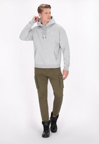 Felpa grigia con cappuccio e tasca frontale, abbinata a pantaloni cargo verde oliva con tasche laterali e stivali neri alti.