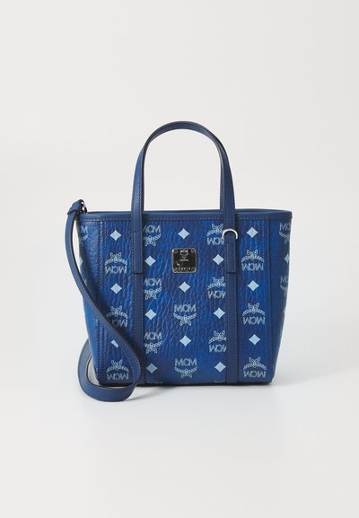 Sac à main en cuir bleu avec finition texturée, arborant un motif de logo MCM et des accents en forme de diamant, deux poignées supérieures et une bandoulière amovible.
