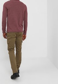 Bordeaux dlouhý rukáv, khaki cargo kalhoty s bočními kapsami a černé boty, viděné zezadu na jednobarevném pozadí.